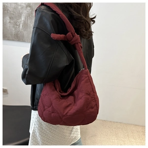 Detail of burgundy heart-quilted tote bag with knotted strap shown on a model