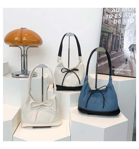Three canvas hobo bags with bow ties in white, black, and denim blue on display