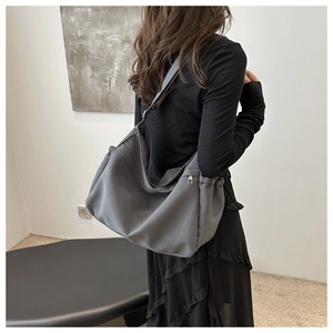 Side view of a grey nylon bucket bag with pleat details and a secure zipper closure