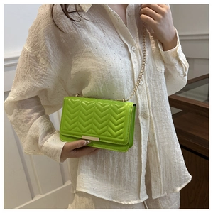 Detail of a bright lime green quilted mini crossbody bag with a fine gold chain strap