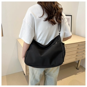 Detail shot of black canvas shoulder bag with adjustable strap worn by a model in a room