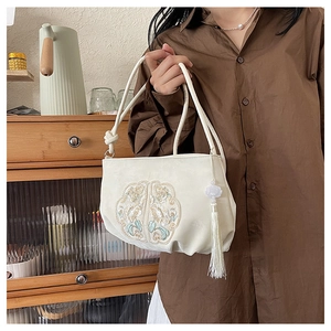 Detail of white silk handbag featuring gold embroidery and elegant white tassel