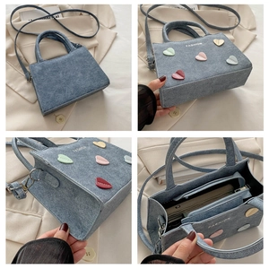 Detail view of denim light blue handbag showing 5 colorful hearts and fashion text