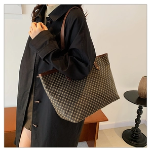 Close-up of a vintage brown checkered tote bag with leather straps on a wooden table