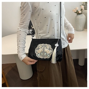 Detail of elegant black velvet bag with gold floral embroidery and white tassel charm