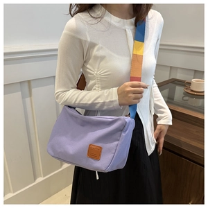 Détail du sac bandoulière en toile violette avec sangle rayée colorée et empiècement cuir
