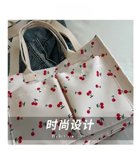 Detail shot of the red cherry print on white canvas tote with functional front pockets
