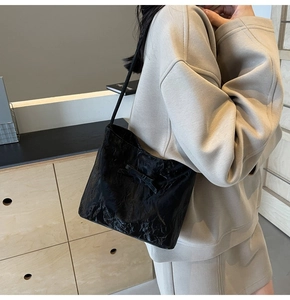 Detail of black pleated tote bag with bow detail and thin shoulder strap worn by model