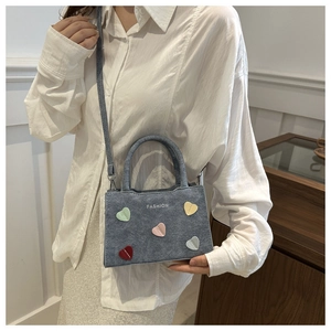 Blue denim handbag with colorful hearts and adjustable strap shown on a female model