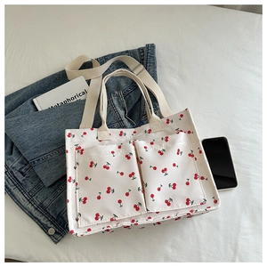 Detailed view of white canvas tote bag with cherry prints and dual front pockets