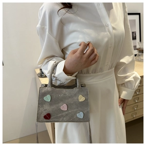 Detail view of a gray crossbody bag featuring a colorful heart pattern and fashion text