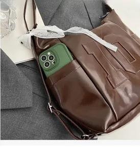 Détail du sac cabas marron brillant avec poche frontale et nœud en dentelle blanche