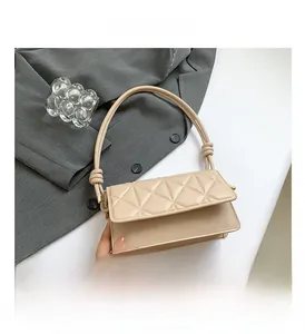 Detail of beige quilted shoulder bag with knot strap on grey suit jacket background
