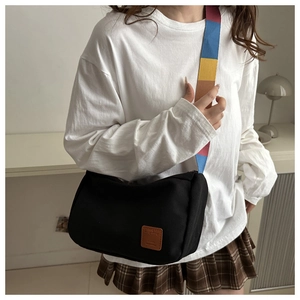Détail d'un sac bandoulière en toile noire avec une large bandoulière rayée multicolore vive