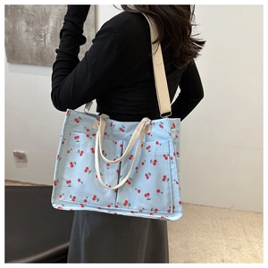 Detail of light blue canvas cherry tote bag featuring two front pockets and detachable strap