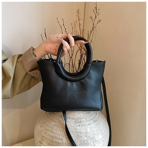 Detail of black pebbled leather handbag with unique round metal handle and long strap