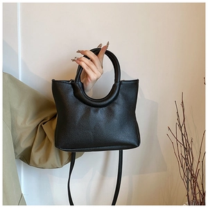 Close-up of black litchi pattern leather handbag with unique circular handle and strap