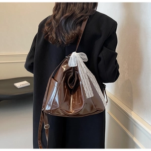 Détail du sac cabas marron brillant avec nœud en dentelle blanche et boucle en métal