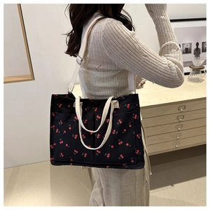 Detail of black canvas tote bag with red cherry prints and white adjustable strap