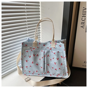 Detail of light blue cherry print canvas tote bag with front pockets and adjustable strap