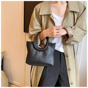 Detail of black lychee grain leather handbag with minimalist circular cutout handle