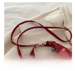 Close-up of glossy red crescent bag with silver clover charm on a beige suit