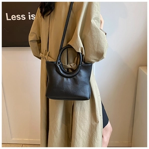 Detail shot of a black litchi pattern leather handbag paired with a beige trench coat