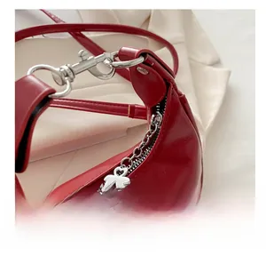 Macro detail of red crescent bag showing silver zipper and clover charm accessory