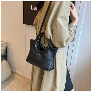 Detail of black lychee grain leather handbag with circular handle and long strap