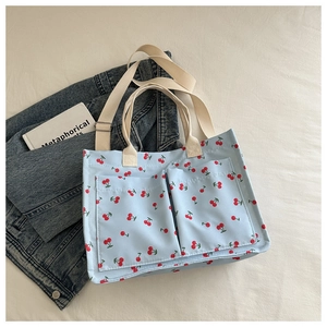 Detail of light blue canvas tote with cherry prints showing front pockets and denim texture