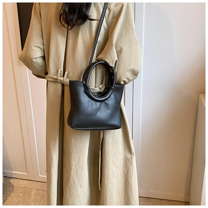 Detail of black pebbled leather handbag with unique round handle and adjustable strap