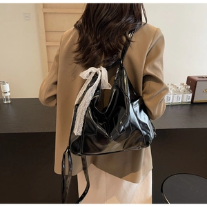 Détail d'un sac cabas en cuir verni noir brillant avec un nœud en dentelle blanche