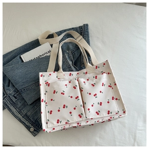 Close-up of white canvas tote bag featuring red cherry prints and dual front pockets