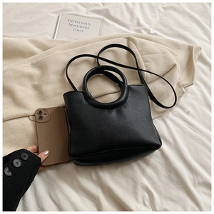 Detail of black lychee-grain leather handbag with round handle and slender strap