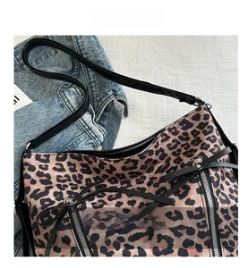 Close-up of leopard print shoulder bag with zipper detail and long strap on denim