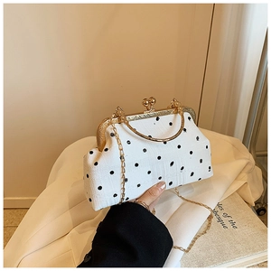Close-up of retro white polka dot handbag with gold frame on a beige blazer background
