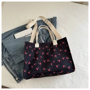 Detail of navy canvas tote bag with red cherry print featuring adjustable shoulder strap