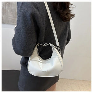 Detail view of a white glossy crescent hobo bag worn by a model with a thin strap