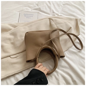 Detail of tan lychee grain leather handbag with circular handle and thin strap on fabric