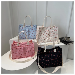 Detail of canvas tote bags with cherry prints, featuring front pockets and straps