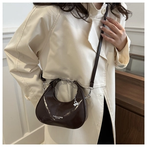 Coffee brown patent leather crescent bag worn crossbody with silver clover charm