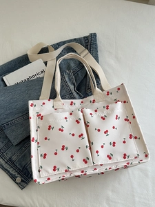 White canvas tote bag with red cherry print featuring double front pockets and shoulder strap