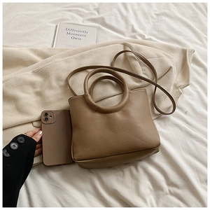 Close-up of brown litchi grain leather handbag with round handle and slender strap
