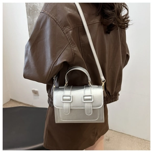 Detail of silver metallic crossbody bag featuring double buckle straps and hand strap