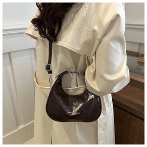 Close-up of dark brown crescent bag with clover charm and silver zipper detail