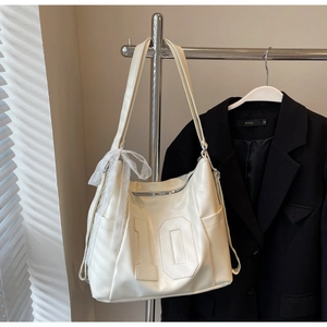Détail d'un sac cabas beige montrant le chiffre 10 embossé et un nœud décoratif en dentelle
