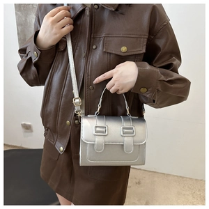 Detail view of small silver square handbag featuring double decorative buckle straps
