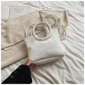Close-up of minimalist white lychee pattern leather handbag with ring handles on soft bed