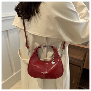 Detail showing the red glossy patent leather crescent bag with chic pleats and silver charm