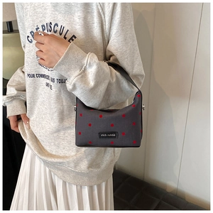 Gros plan d'un sac en toile gris à pois rouges avec étiquette de marque porté par un mannequin